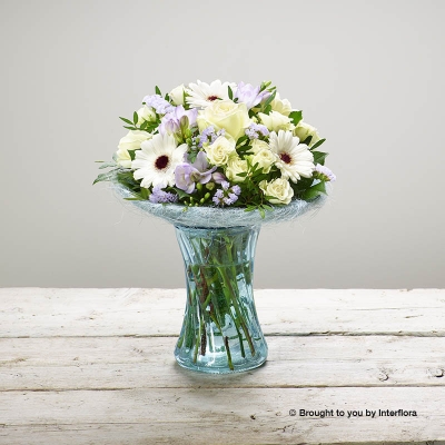 White Germini Ivory rose White Spray Rose Purple Freesia Lilac Statice & Greenery in Blue Glass Vase